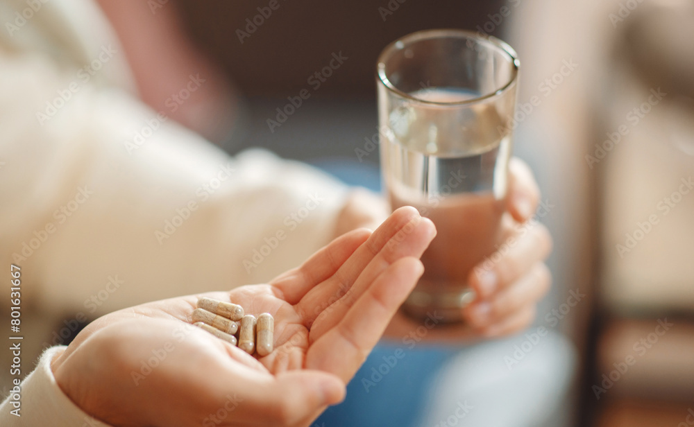 A close-up view illustrates man holding several pills in one hand and clear glass of water in the other, preparing to take medication. The focus on the hands conveys an everyday healthcare routine. A close-up view illustrates man holding several pills in one hand and clear glass of water in the other, preparing to take medication. The focus on the hands conveys an everyday healthcare routine.