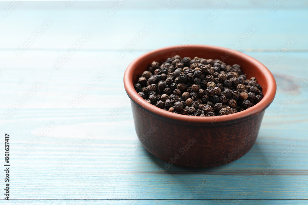 Aromatic spice. Black pepper in bowl on light blue wooden table, space for text Aromatic spice. Black pepper in bowl on light blue wooden table, space for text