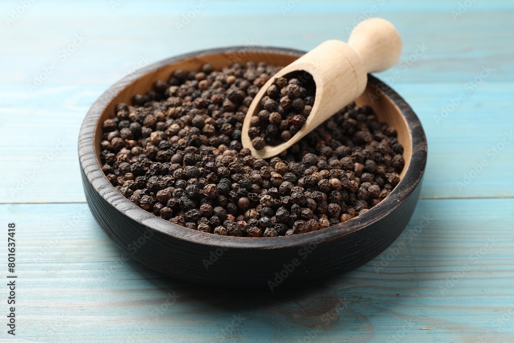 Aromatic spice. Black pepper in bowl and scoop on light blue wooden table Aromatic spice. Black pepper in bowl and scoop on light blue wooden table