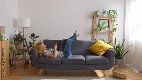 Full angle view of happy young caucasian woman using mobile phone while lying a couch at home. photo