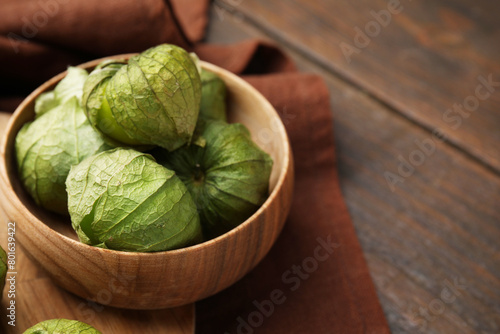 Fresh green tomatillos with husk in bowl on wooden table, closeup. Space for text photo