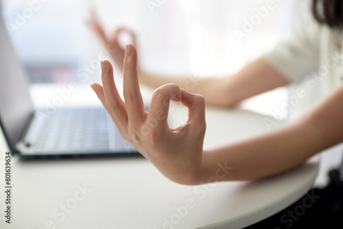 Close up image of woman's hands who was sitting and meditating at his desk in a white office To meditate to calm the mind and relax before starting work. The room is bright with natural light.