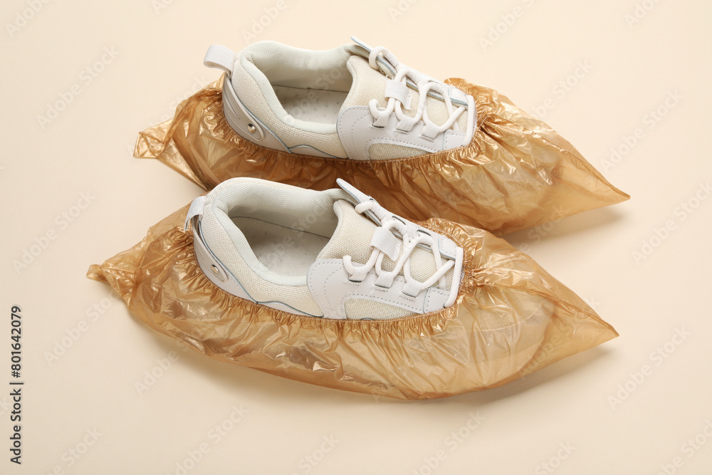 Sneakers in shoe covers on beige background, closeup Sneakers in shoe covers on beige background, closeup