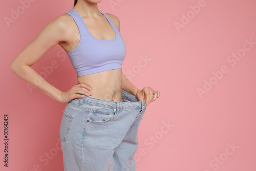 Woman in big jeans showing her slim body on pink background, closeup. Space for text