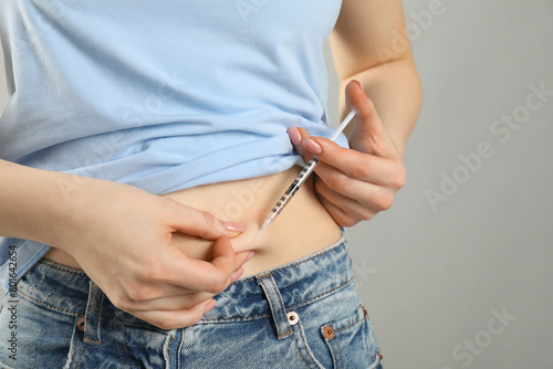 Diabetes. Woman making insulin injection into her belly on grey background, closeup