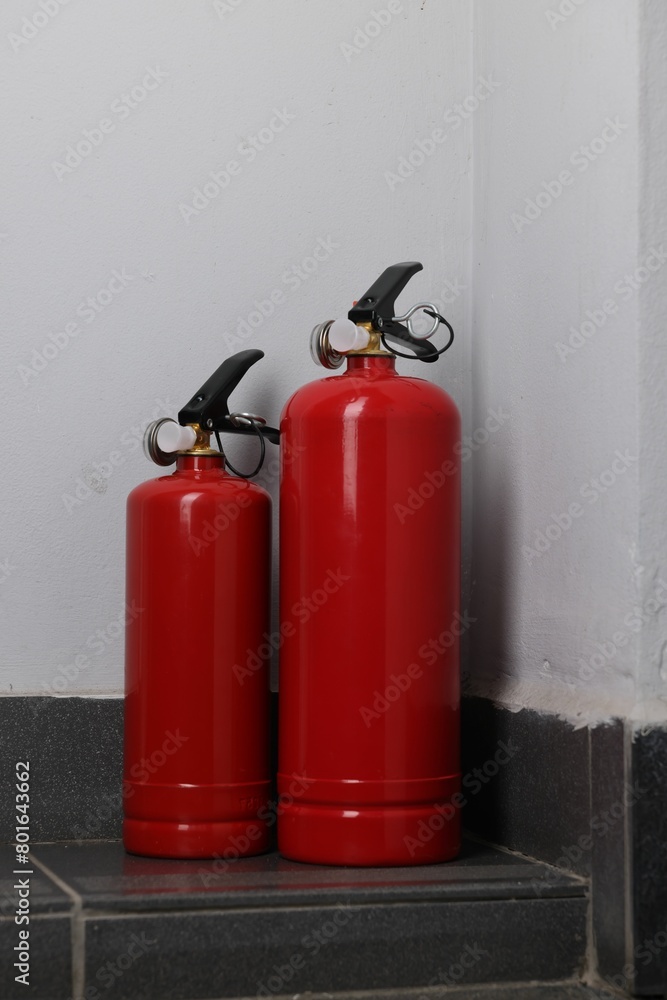 Two fire extinguishers on floor near white wall Two fire extinguishers on floor near white wall