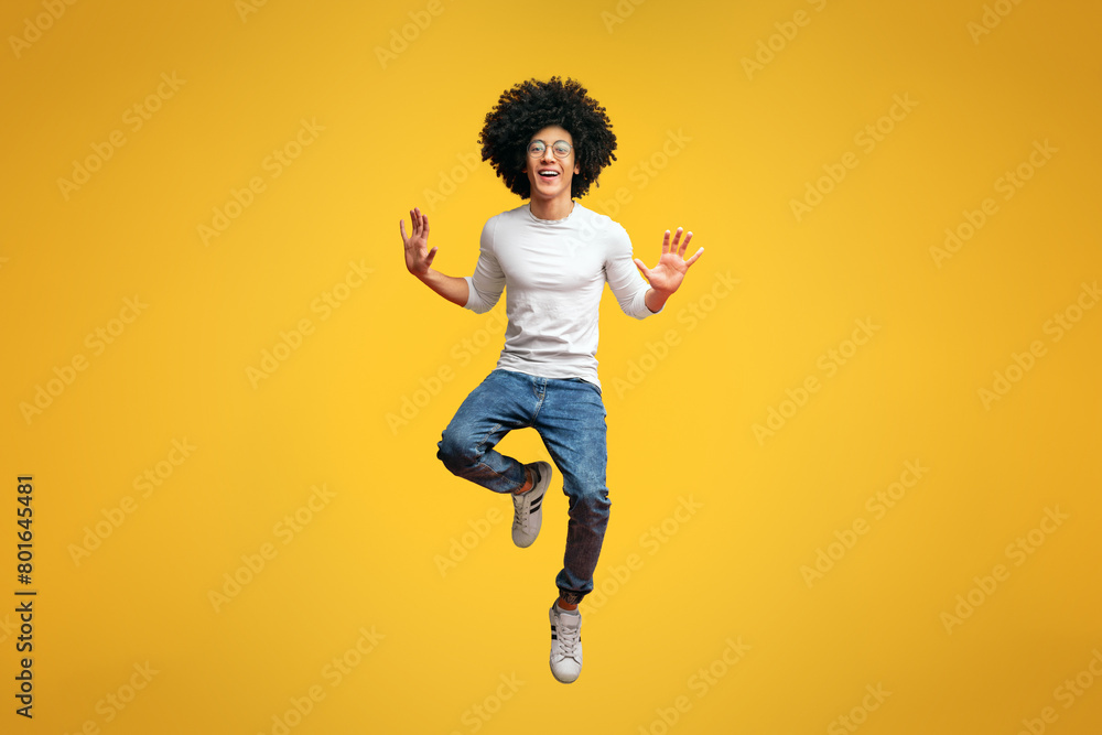 Obraz premium Cheerful millennial guy fooling, jumping in air on orange studio background