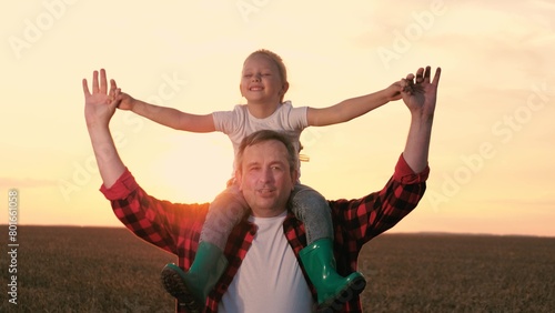 Smiling father and daughter walking at sunset agriculture wheat field closeup. Cute little girl sitting on male parent shoulders with open hands enjoy freedom happy childhood sunrise sky meadow © DREAM INSPIRATION