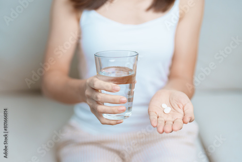 woman hand holding medicine painkiller pill and water glass on the sofa at home, taking for headaches, stomach ache, Diarrhea Pain from food poisoning, Endometriosis, Hysterectomy and Menstrual photo