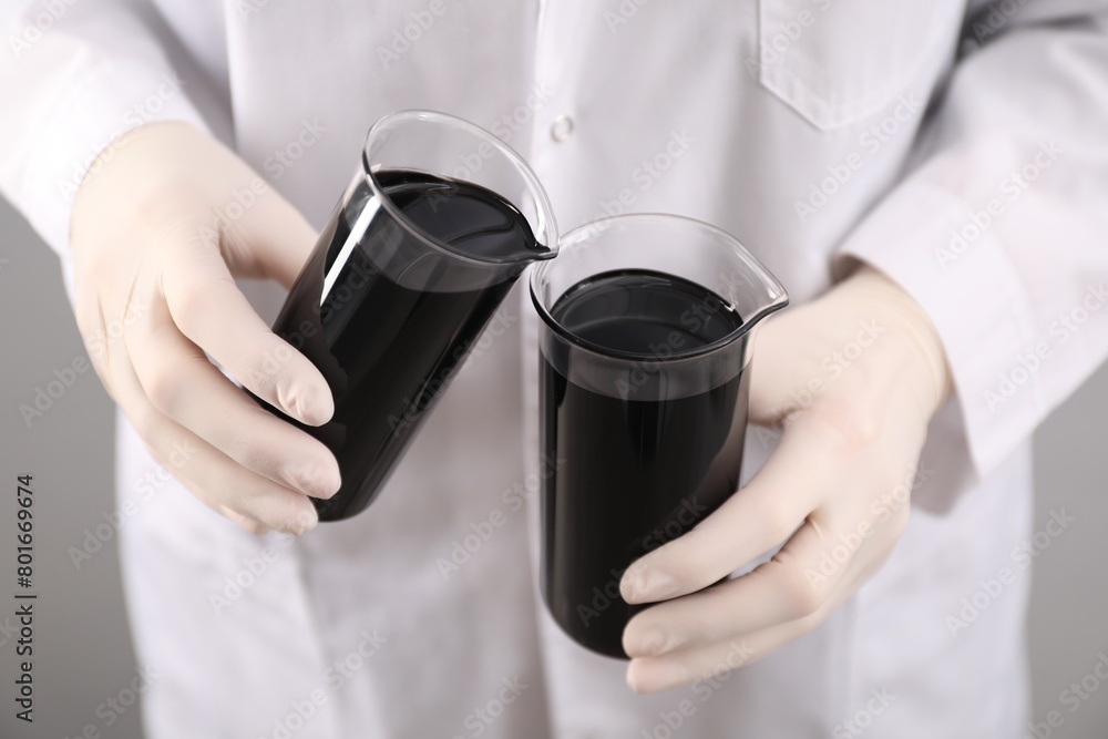 Woman pouring black crude oil into beaker on light background, closeup Woman pouring black crude oil into beaker on light background, closeup
