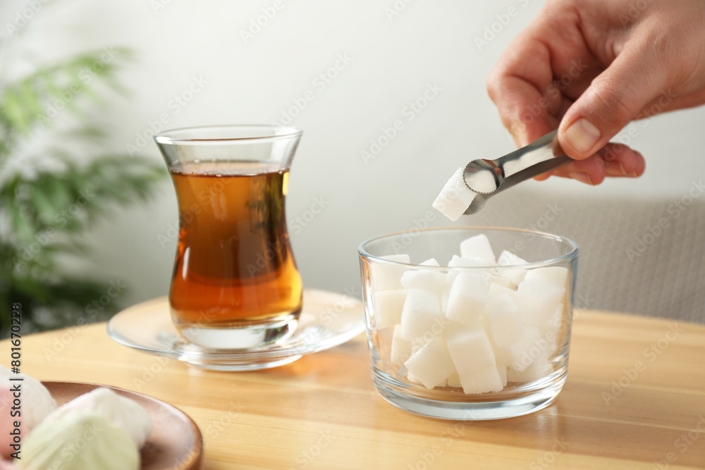 Woman adding sugar cube into aromatic tea at wooden table indoors, closeup Woman adding sugar cube into aromatic tea at wooden table indoors, closeup