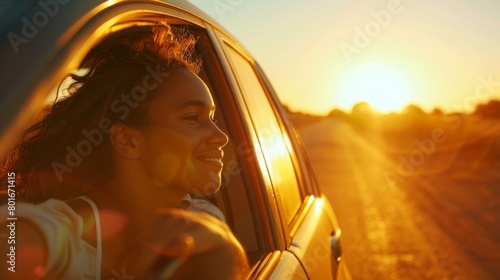 Radiant young African American woman feeling the wind in her hair during a serene sunset car ride, her joyful demeanor framed by warm sunlight.