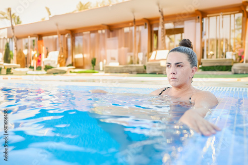 Young woman with a bun in her hair on vacation at a luxury resort takes a swim in the pool