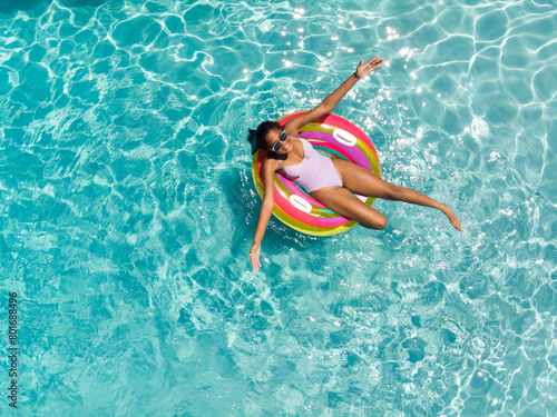 Teenage biracial girl enjoys a sunny day in the pool, with copy space