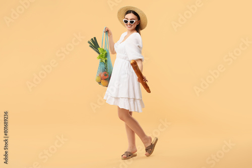 Woman with string bag of fresh vegetables and baguette on beige background