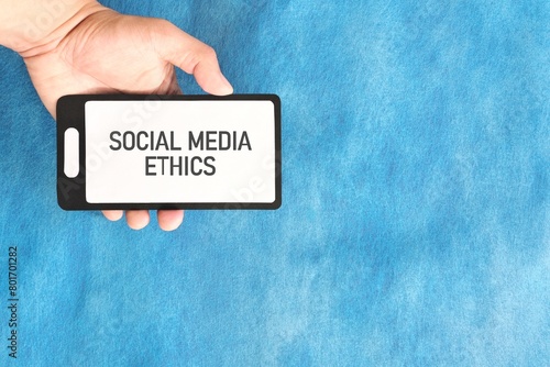 Social media ethics concept. Human hand holding mobile phone on blue background.