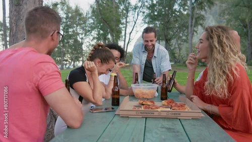 Amidst shared laughter and cheerful conversation, friends enjoy slices of pizza and cold drinks at an outdoor table, creating lasting memories in a friendly atmosphere. Slow motion.  photo