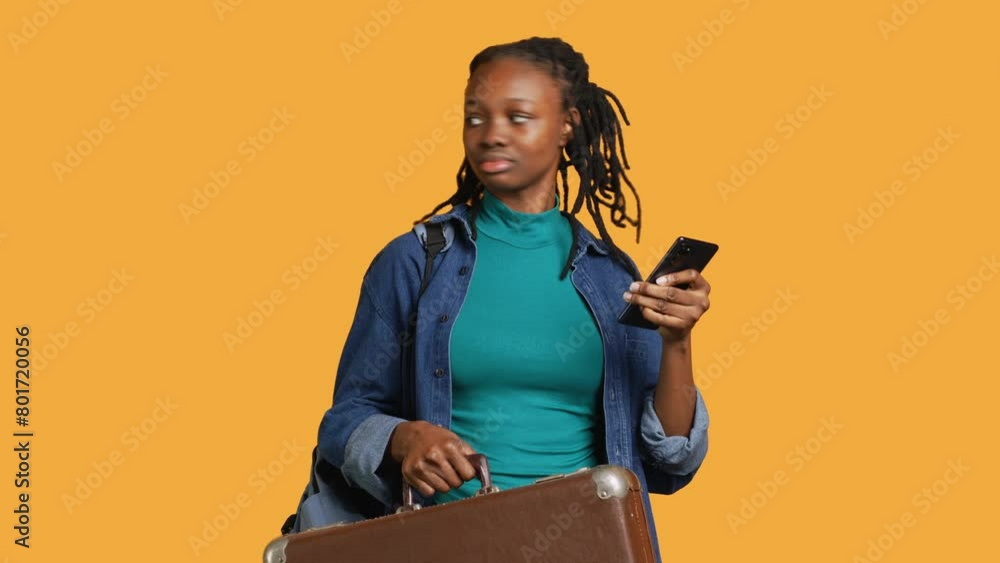 Smiling girl going on vacation, holding suitcase, reading texts on phone. Cheerful woman with luggage in hands texting on cellphone, isolated over studio background, camera A Smiling girl going on vacation, holding suitcase, reading texts on phone. Cheerful woman with luggage in hands texting on cellphone, isolated over studio background, camera A
