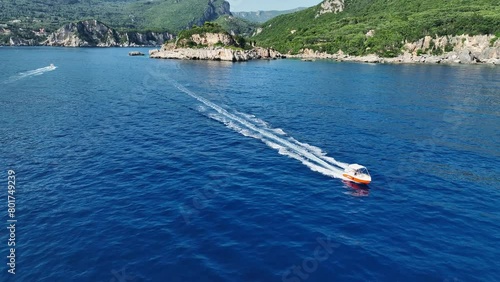 Speedboat cutting through blue waters near Corfu Island with cliffy coast in the background, aerial view photo