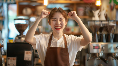 A female coffee shop employee stands in front of the camera with a bright smile and pumps both fists as if cheering