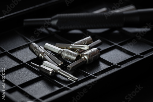 Torx drive bit and aluminum bit driver on black sorting tray. Screws and drive bits. Screwdriver handle with magnetic bit socket and knurled grip.
