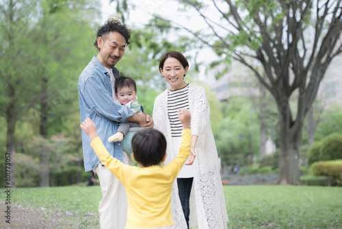 逆光の新緑の公園で遊ぶ仲良しで笑顔の日本人家族　パパとママに駆け寄る子供