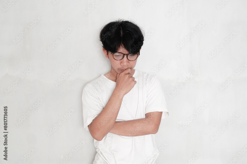 asian man in casual clothes and glasses thinking and doubting, holding his chin with hand on white studio background asian man in casual clothes and glasses thinking and doubting, holding his chin with hand on white studio background