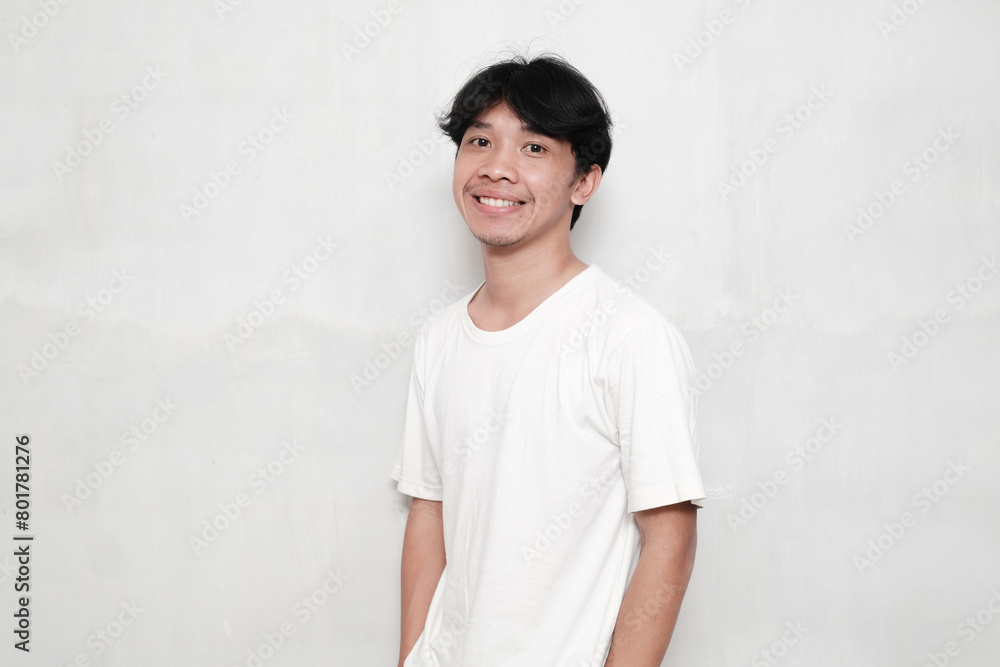 Confident Man. Portrait of smiling Asian man wearing blank white t-shirt for design print mockup, standing isolated over white studio background. Happy casual male model laughing looking at the camera Confident Man. Portrait of smiling Asian man wearing blank white t-shirt for design print mockup, standing isolated over white studio background. Happy casual male model laughing looking at the camera