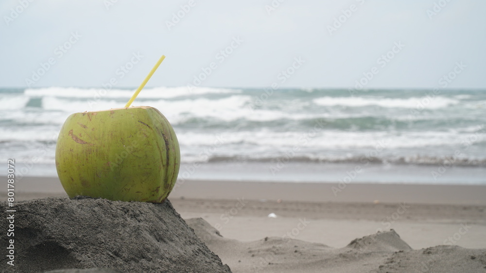 Coconut fruit with straw on beach sand. Blur sand and waves background. Focus selected Coconut fruit with straw on beach sand. Blur sand and waves background. Focus selected