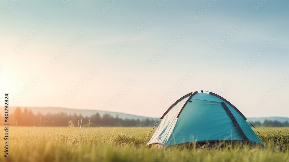Early morning camping scene with a tent in a field under a clear sunrise sky.