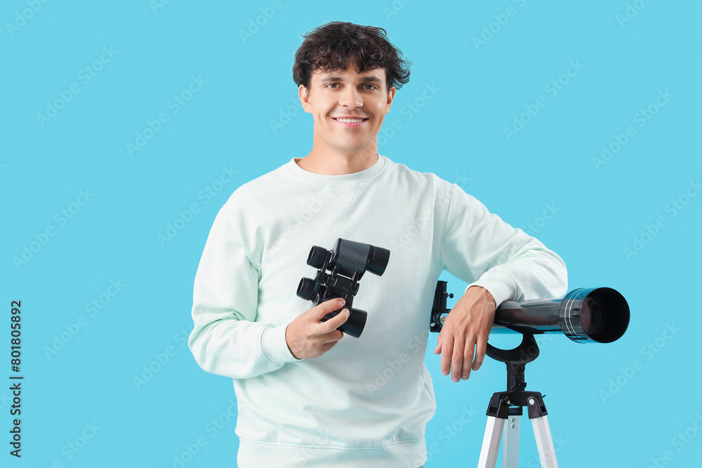 Obraz premium Young man with telescope and binoculars on blue background