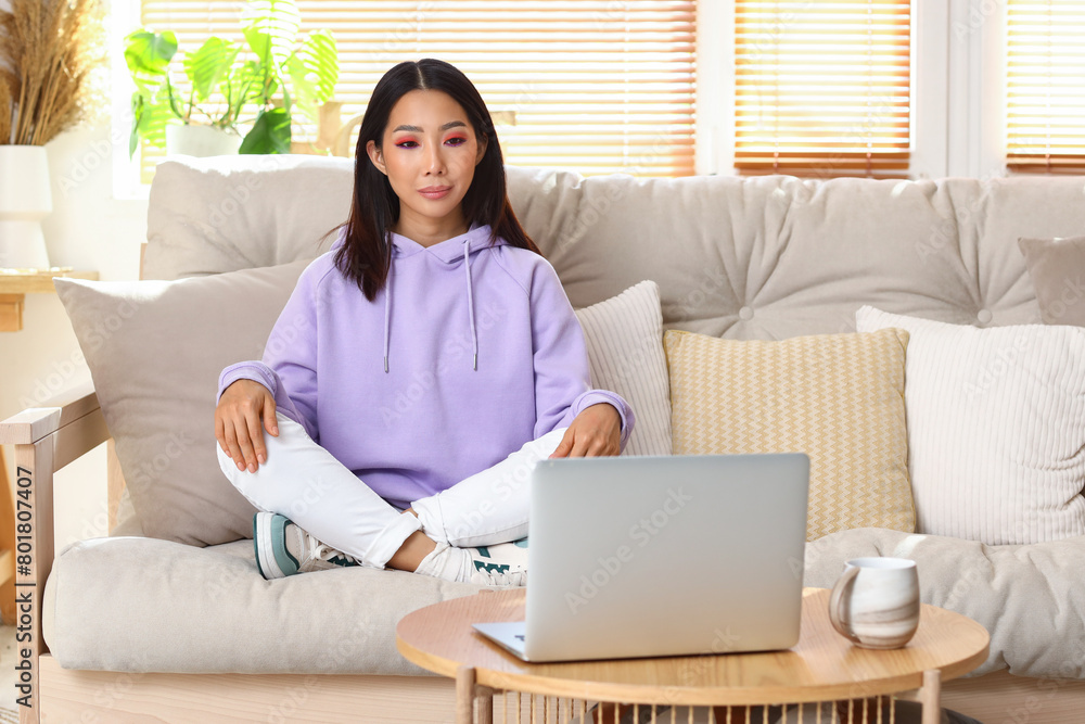 Young Asian woman in hoodie sitting on sofa at home Young Asian woman in hoodie sitting on sofa at home