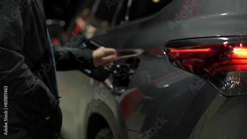 person refueling their car during nighttime, with the car's taillights glowing warmly. The scene emphasizes the routine yet essential task of refueling, highlighting the practical aspects of car maint photo