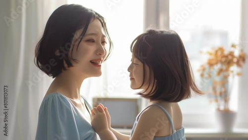 Smiling young mother in blue outfit lovingly dances with her little daughter in matching dress, sharing a heartwarming moment of joy and connection at home by the window.
 photo