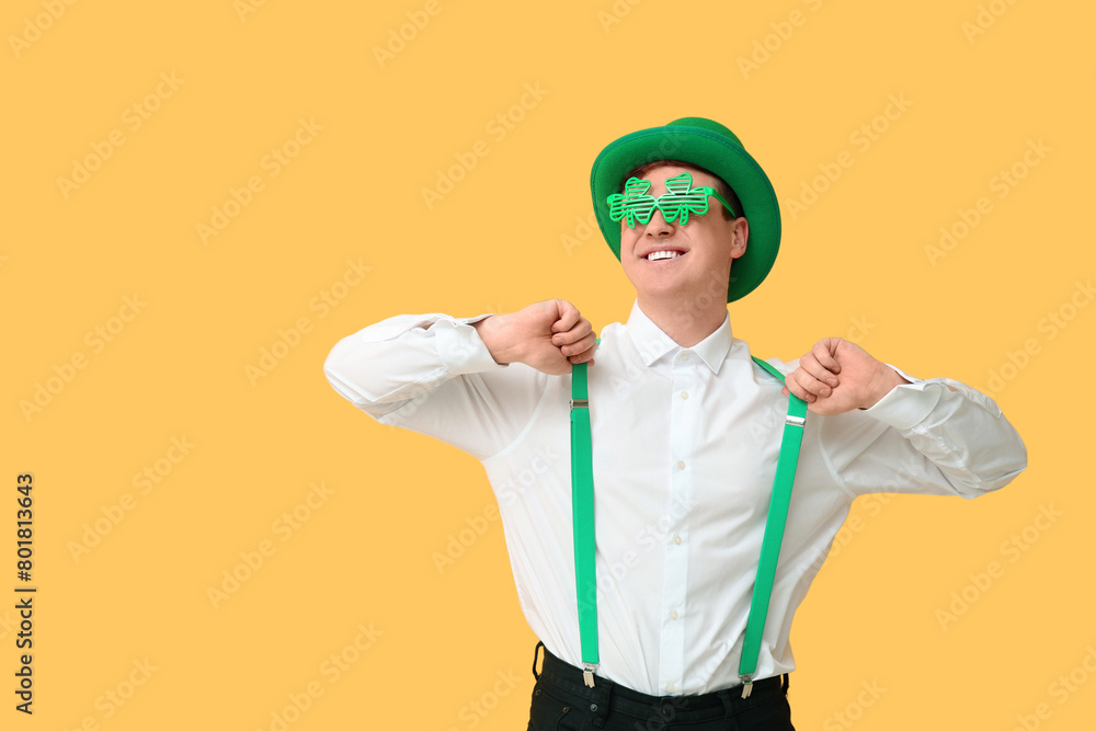 Happy young man in leprechaun's hat with party glasses on yellow background. St. Patrick's Day celebration