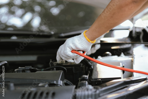 Close-up of auto mechanic charging car battery with electric rail jumper cables 