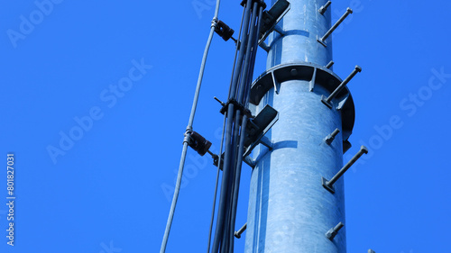 Cables and ground wires on telephone base poles. Closeup of group of wires on rack on metal pole of 4G or 5G telecommunication substation on blue sky background with copy space with selective focus.