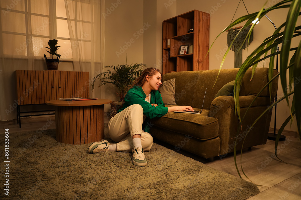 © Pixel-Shot - Young woman using laptop on sofa at home in evening