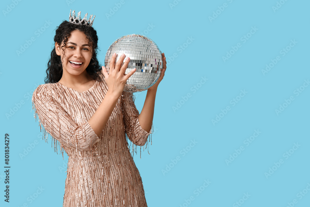 Naklejka premium Beautiful young African-American woman in tiara and stylish dress with disco ball on blue background