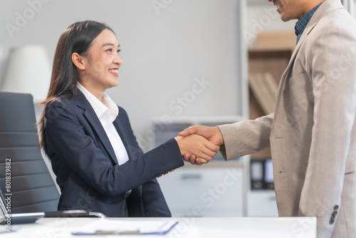 Young Asian businesswoman and middle-aged businessman, exemplifying pivotal moments, clear articulation, proliferation of ideas, and overcoming divisive challenges with successful handshakes.