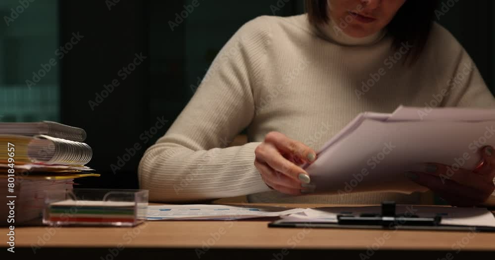Accountant manager sits at table and looks through documents in evening Accountant manager sits at table and looks through documents in evening