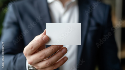 A business man in a suit holds out an empty white card for a mockup