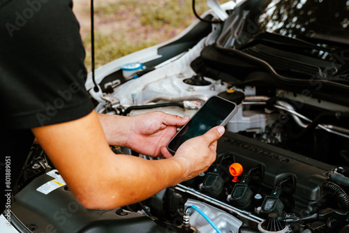 Fotografie Mechanic uses smartphone to inspect car engine parts
