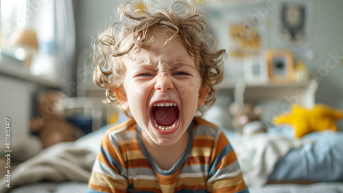 A 4-year-old boy screams against the background of a children's bedroom. toddler having a temper tantrum in their bedroom. The little boy is angry. children's bad sleep photo