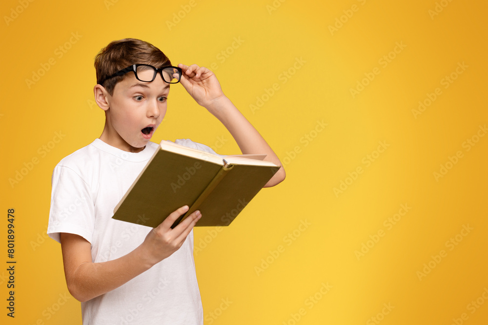 A young boy wearing glasses is engrossed in reading a book. A young boy wearing glasses is engrossed in reading a book.