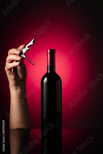 Unopened bottle of red wine and hands with corkscrew.