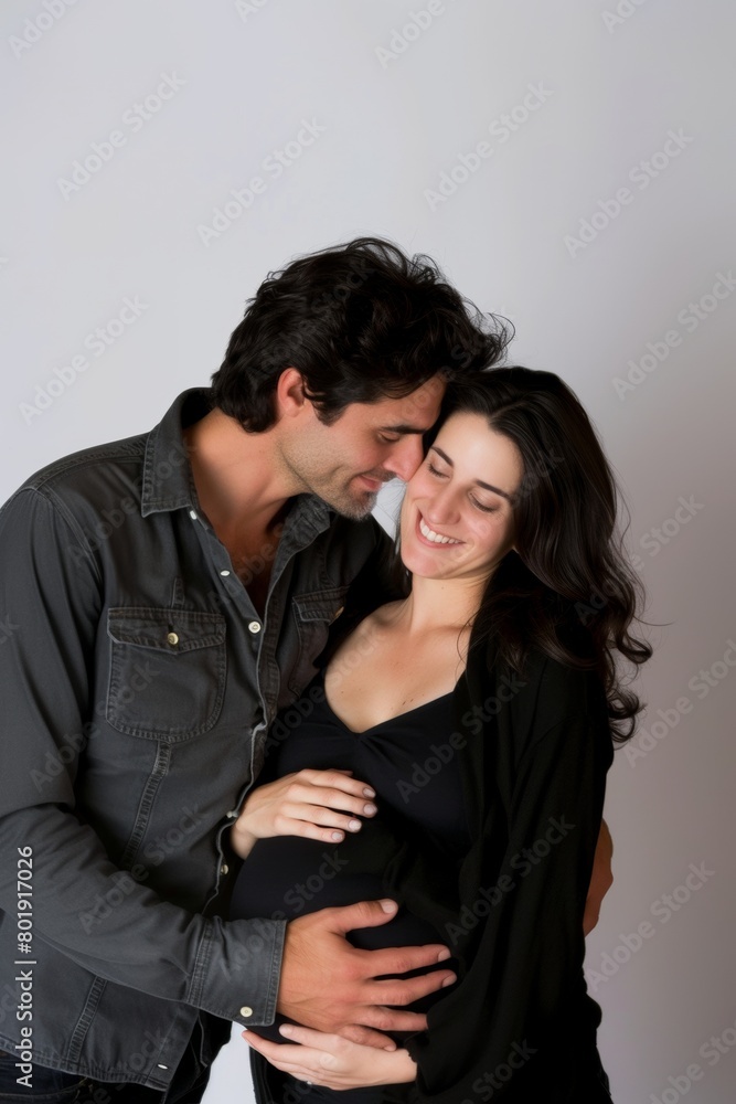 Expectant couple sharing a loving moment, with hands on the pregnant belly, standing against a neutral background. Expectant couple sharing a loving moment, with hands on the pregnant belly, standing against a neutral background.
