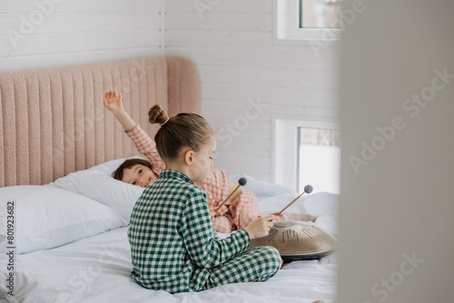 little daughters play in the bedroom on their parents' bed, playing the glucophone