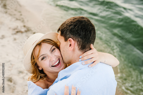 Couple in love hugging and kissing on seashore. Male kisses female on cheek on beach ocean and enjoys sunny summer day. Man embraces woman on sand sea. Spending time together. Closeup face. Top view © Serhii