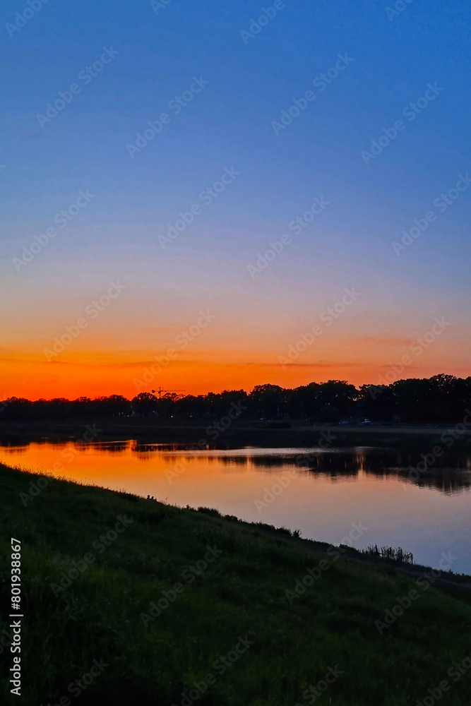 Naklejka premium Tranquil Sunset Over Serene River with Lush Riverside